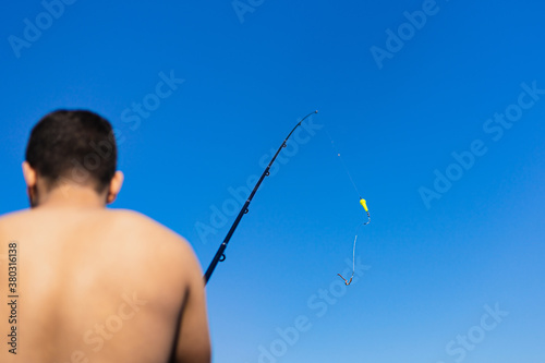 Young dark short-haired man of Maghreb origin fishing on his back, with the fishing rod raised in the foreground.