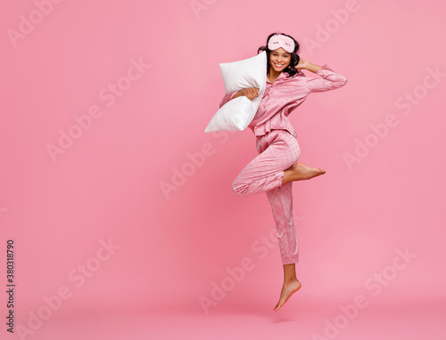 Excited woman in pajama jumping with pillow. photo