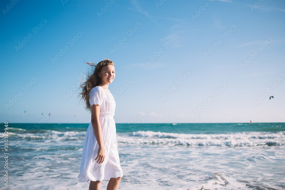 Happy stylish girl standing on beach against waving sea Happy stylish girl standing on beach against waving sea