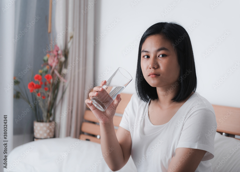 Beautiful Asian woman drinking fresh water from glass in white bedroom interior background Beautiful Asian woman drinking fresh water from glass in white bedroom interior background