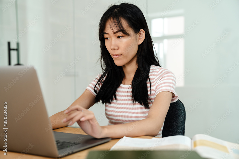 Photo of asian girl doing homework with laptops while sitting at table Photo of asian girl doing homework with laptops while sitting at table