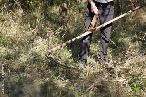 Fototapeta Man with scythe in the garden, grass is mowed and cut by hand.