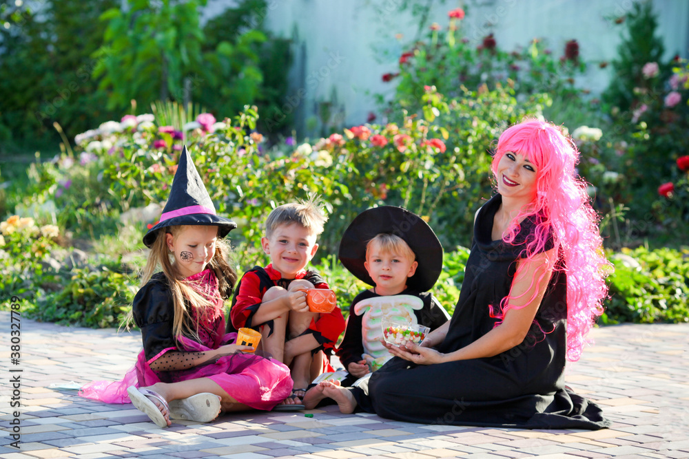 Fototapeta premium Young kids trick or treating during Halloween . Children and a woman are sitting on the road in halloween costumes.