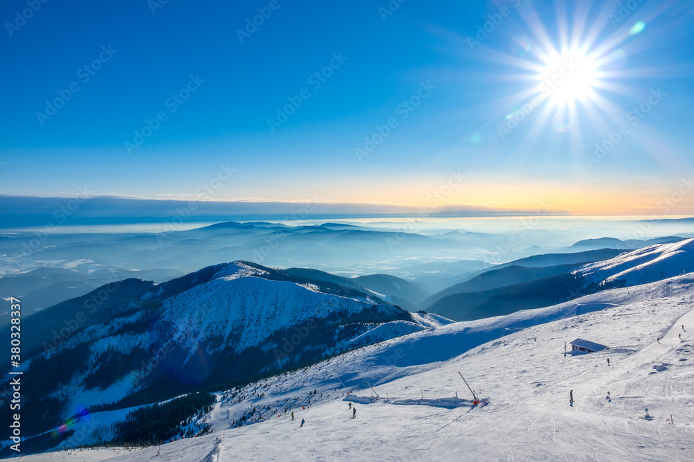Ski Slope and Winter Sun over Mountain Peaks