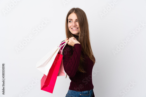 Young woman over isolated white background holding shopping bags and looking back