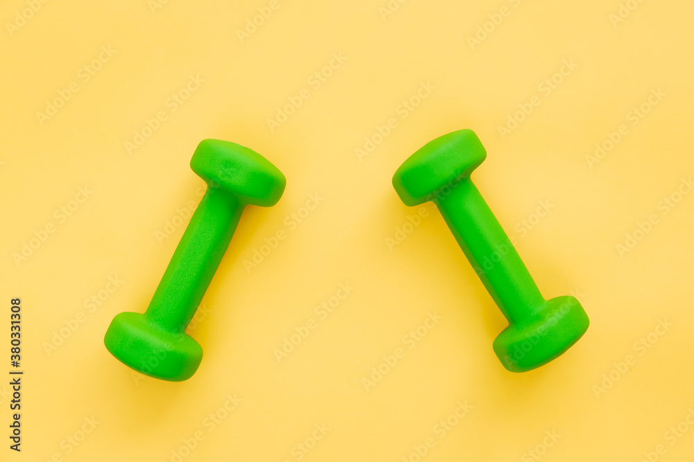 Pair of green female dumbbells on yellow background. Healthy lifestyle, home workout concept. Space for text. Pair of green female dumbbells on yellow background. Healthy lifestyle, home workout concept. Space for text.