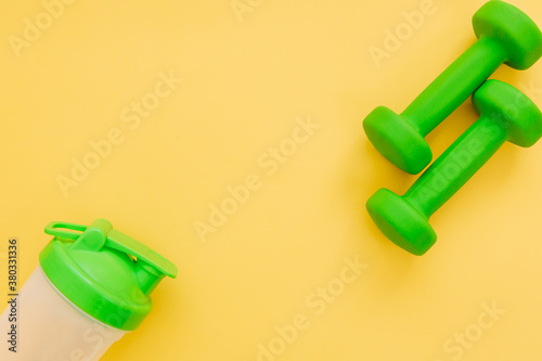 Green dumbbells and bottle for water on yellow background. Healthy lifestyle, fitness concept. Space for text. 