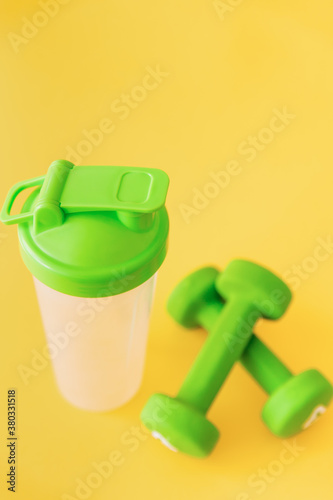 Pair of green dumbbells and bottle for water on yellow background. Healthy lifestyle, fitness concept. Selective focus.