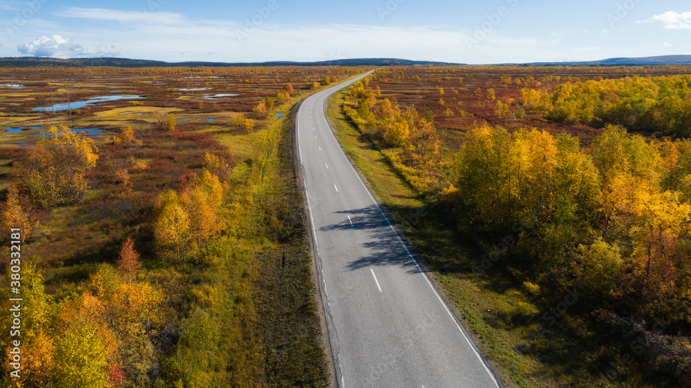 Aerial view of road and forest in autumn colors. Highway to Lapland. Beautiful landscape with rural road and trees with colorful leaves. Ruska fall season in Finland.