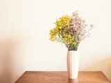Dried pink and yellow flowers in white vase against white wall. Home interior autumn decor