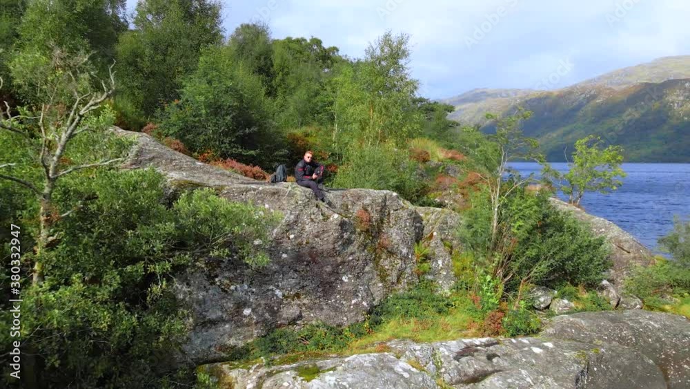 Zooming out from a person sitting on the rock to reveal Loch Lomond lake and mountains from the air in the summer.
Zooming out from a person sitting on the rock to reveal Loch Lomond lake and mountains from the air in the summer.