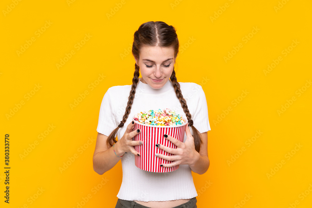 Young woman over isolated yellow background holding a big bucket of popcorns Young woman over isolated yellow background holding a big bucket of popcorns