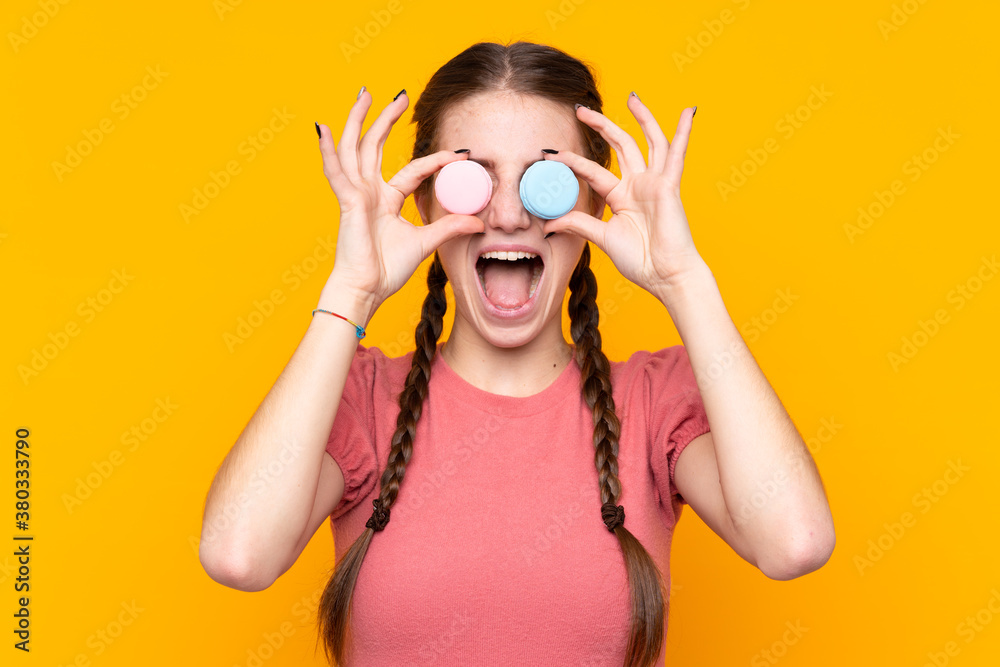 Young woman over isolated yellow background holding colorful French macarons