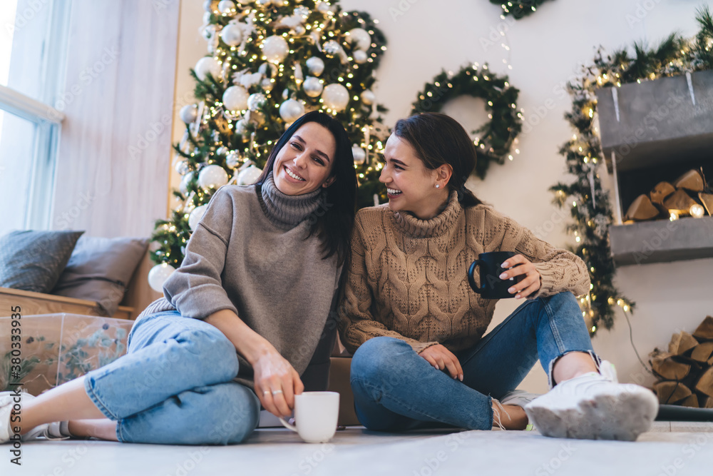 Positive multiethnic young women relaxing with cups of coffee during Christmas holidays at home