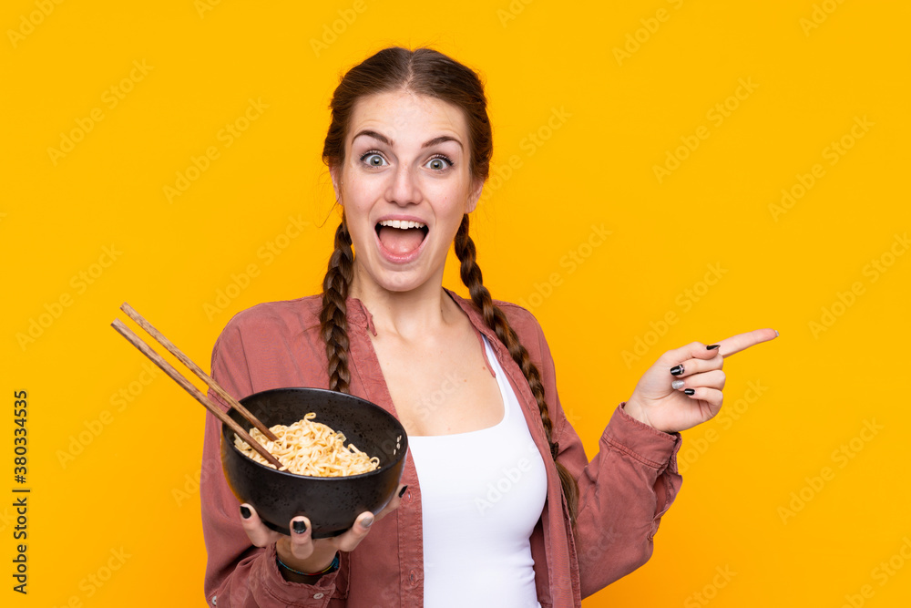 Young woman over isolated yellow background holding a bowl of noodles with chopsticks Young woman over isolated yellow background holding a bowl of noodles with chopsticks