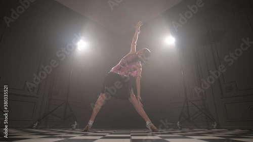 Attractive teenage girl in a beautiful pink black dress professionally dancing ballroom sports dance sambu latino american dances in a dark room filled with smoke photo