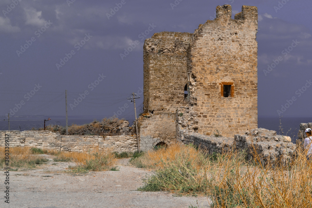 ruin of old ancient stone destroyed tower Genoese fortress in Feodosia made of white sand colored bricks among dry yellow grass. Crimea, summer