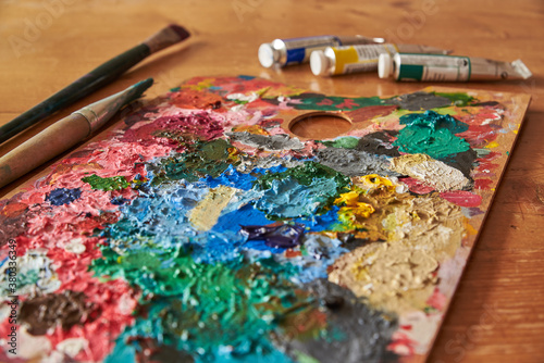 Colorful palette with brushes and oil colors on a wooden table.