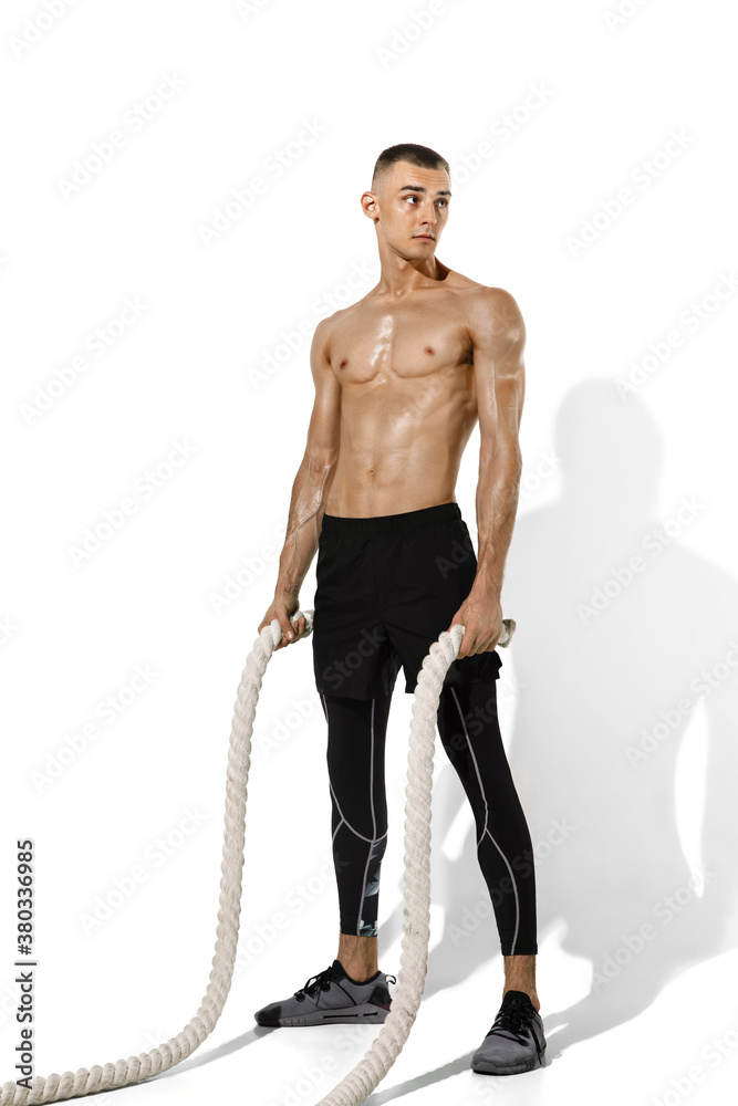 Ropes. Stylish young male athlete practicing on white studio background, portrait with shadows. Sportive fit model in works out in motion and action. Body building, healthy lifestyle, style concept. Ropes. Stylish young male athlete practicing on white studio background, portrait with shadows. Sportive fit model in works out in motion and action. Body building, healthy lifestyle, style concept.