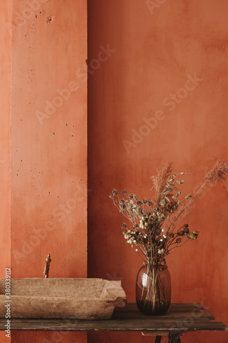 Minimalistic interior style. Dry flowers in a glass vase standing on a wooden shelf with a vintage sink at the orange wall background