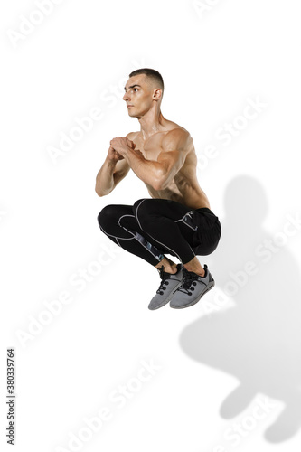 Jumping high. Stylish young male athlete practicing on white studio background with shadows. Sportive fit model in works out in motion and action. Body building, healthy lifestyle, style concept.