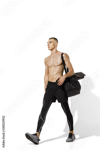 Before workout. Stylish young male athlete on white studio background, portrait with shadows. Sportive fit model in motion and action. Body building, healthy lifestyle, style concept.