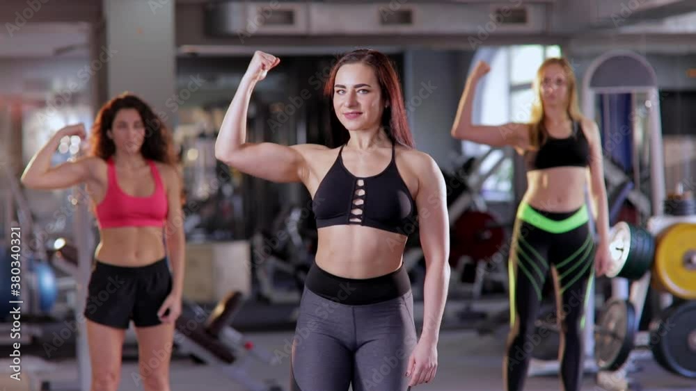 A group of beautiful young toned muscular women in the gym show their biceps and look at the camera. A group of beautiful young toned muscular women in the gym show their biceps and look at the camera.
