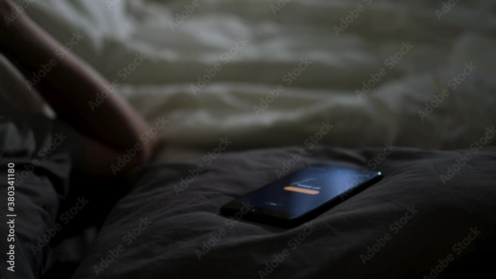 Close up of sleeping man being woken up by his phone lying on the bed. Concept. Male hand trying to turn off the alarm clock lying near on a blanket at home early in the morning.
