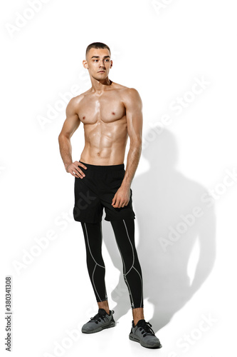 Posing. Stylish young male athlete practicing on white studio background, portrait with shadows. Sportive fit model in works out in motion and action. Body building, healthy lifestyle, style concept.