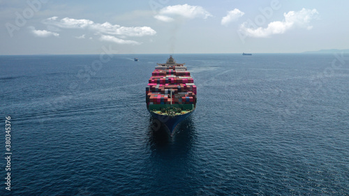 Aerial drone photo of huge container cargo Ship carrying load in truck-size colourful containers cruising deep blue open ocean sea 