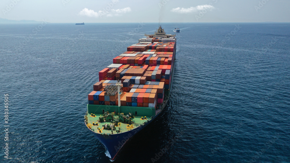 Fototapeta premium Aerial drone photo of huge container cargo Ship carrying load in truck-size colourful containers cruising deep blue open ocean sea 