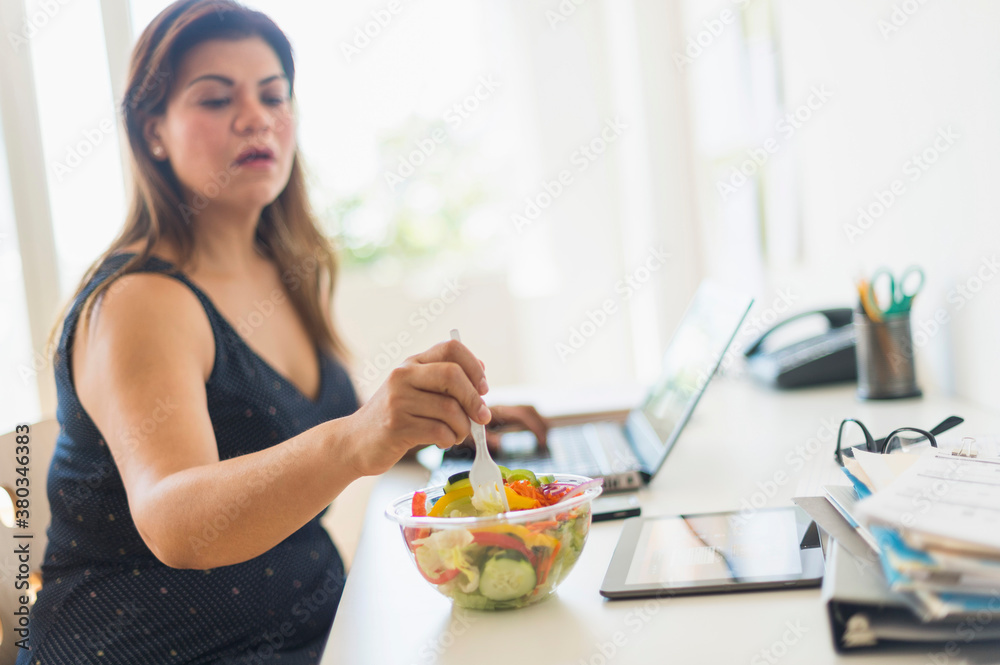 Woman eating salad and using laptop in office Woman eating salad and using laptop in office