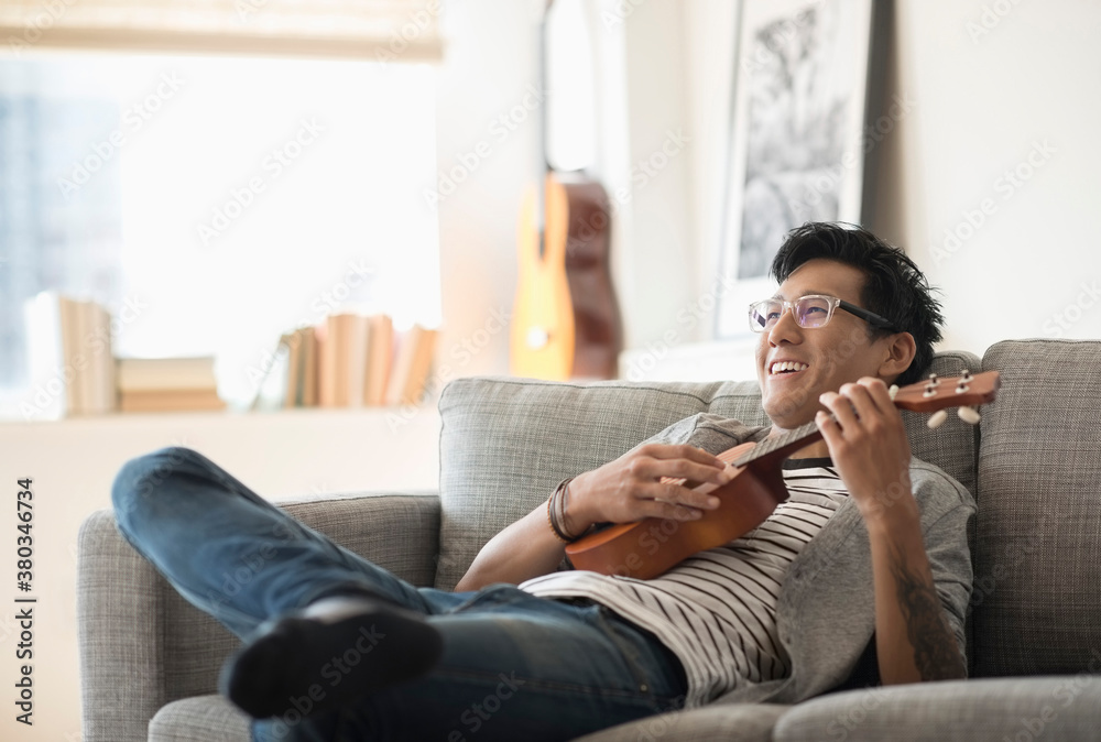 Man sitting on sofa and playing ukulele Man sitting on sofa and playing ukulele