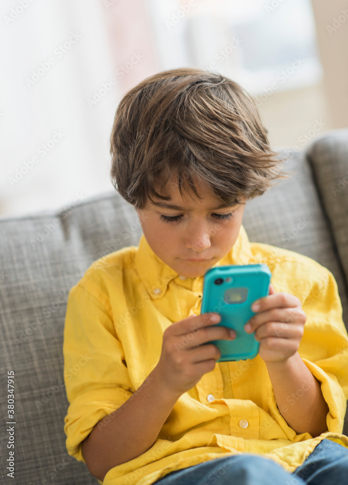 Boy (6-7) sitting on sofa and using cell phone