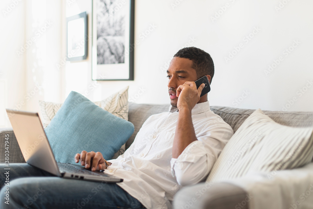 Man sitting in living room, using laptop and cell phone Man sitting in living room, using laptop and cell phone