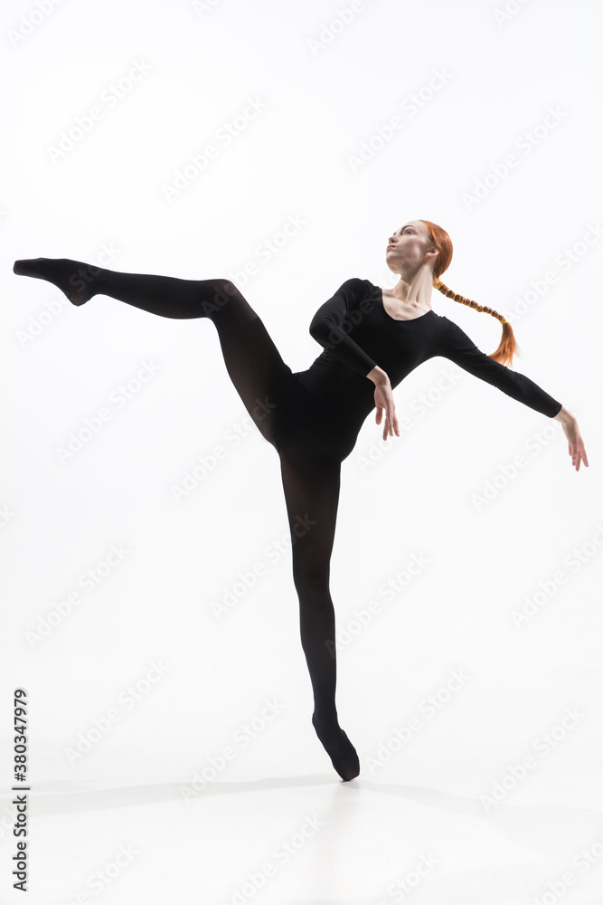 Fototapeta premium Elegance. Young and graceful ballet dancer in minimal black style isolated on white studio background. Art, motion, action, flexibility, inspiration concept. Flexible caucasian ballet dancer.