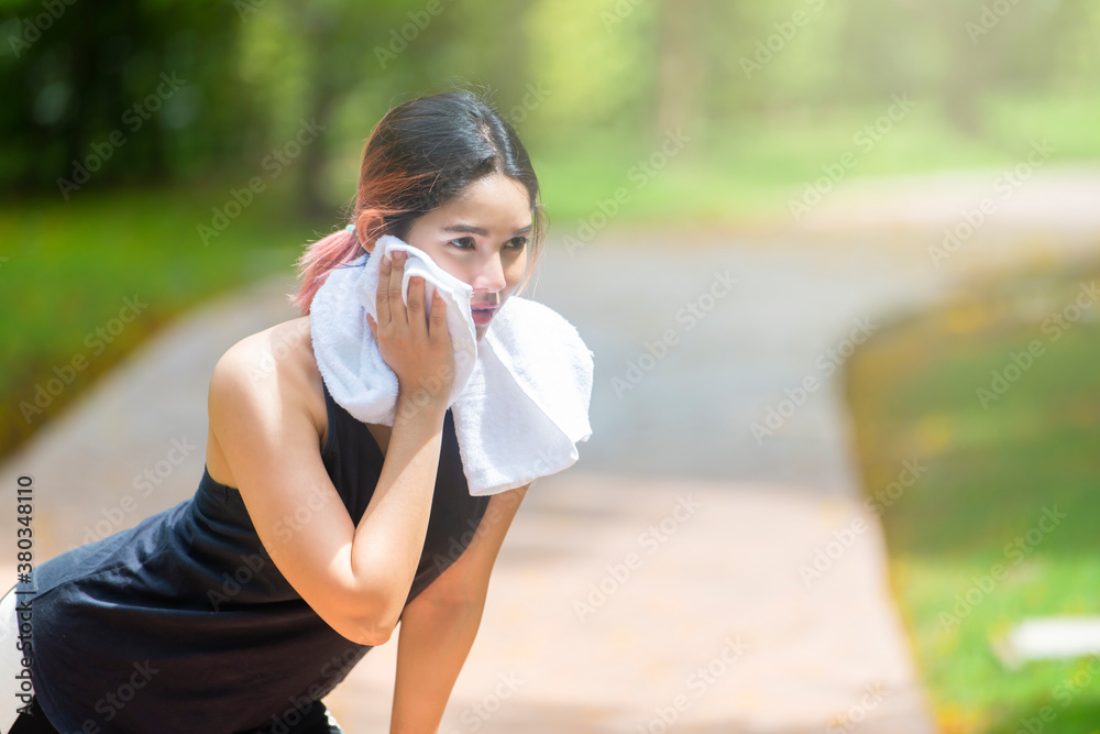 Tired beautiful asian woman after fitness time and exercising in city street park at beautiful summer morning and a white towel to wipe her face. Copy space Tired beautiful asian woman after fitness time and exercising in city street park at beautiful summer morning and a white towel to wipe her face. Copy space