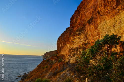 High red yellow sandy long cliffs of Fiolent with green bushes on the Black Sea coast in the light of sunset. Blue water and sky. Gradient on horizon. South Crimea