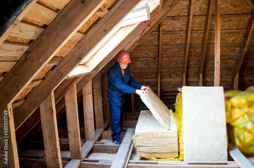 Roof insulation. A worker puts glass wool insulation in the attic.