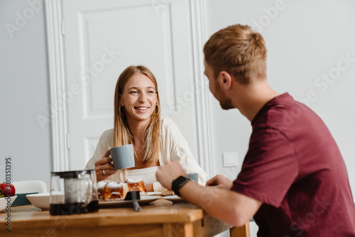 Image of joyful couple drinking coffee with pie while sitting at table