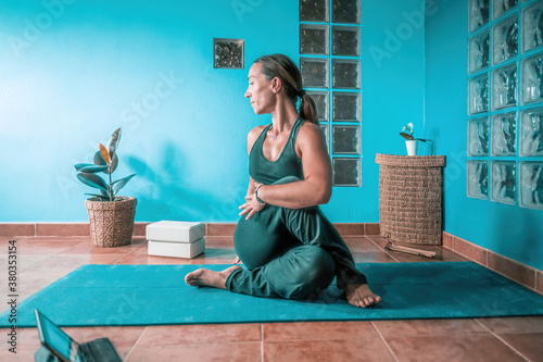 Young latin blonde woman teaching yoga in a online class with the tablet in a blue room with glass tiles and some plants