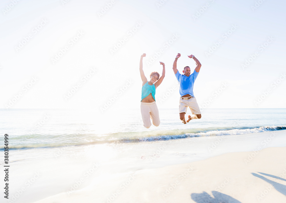 Mature couple jumping in sea with arms raised Mature couple jumping in sea with arms raised