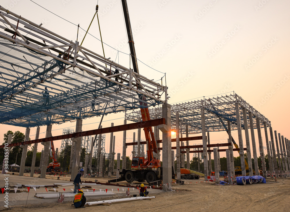 Construction workers are working at height above roof to instrallation accessory steel structure roof truss at construction site factory project during sunset time Construction workers are working at height above roof to instrallation accessory steel structure roof truss at construction site factory project during sunset time