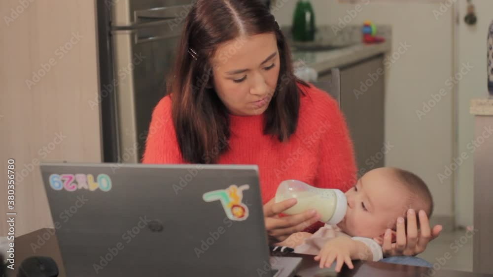 Mujer joven mexicana trabajando desde casa con computadora en comedor dando de comer a bebe