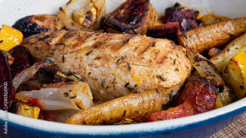 A grilled chicken is sitting in a ceramic plate alongside various root vegetables. The marks from the iron skillet is clearly visible as charred lines on the breast.
