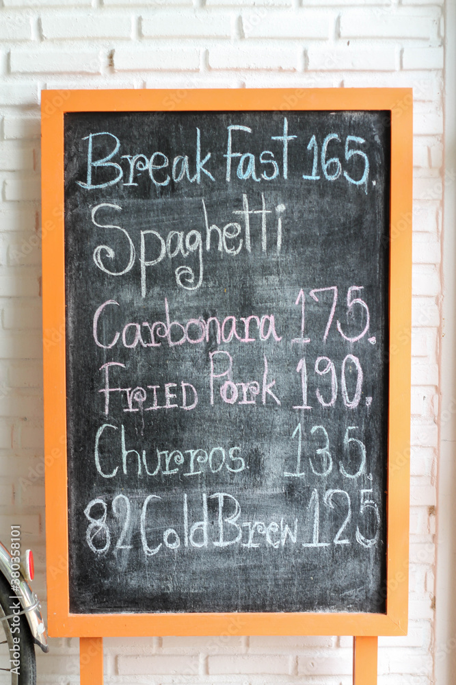 Naklejka premium Handwritten menu on chalkboard in front of white brick wall.