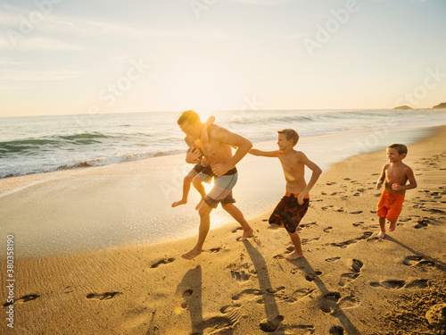 Father playing football on beach with his three sons (6-7, 10-11, 14-15)