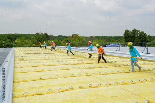 Construction workers teamwork are working installation metal roof sheet new warehouse at construction site factory project