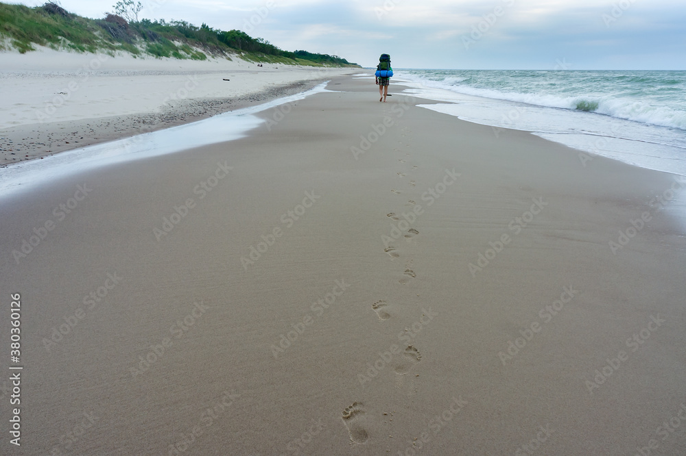 A tourist walks along the sea coast, Baltic sea. A man with a large backpack.