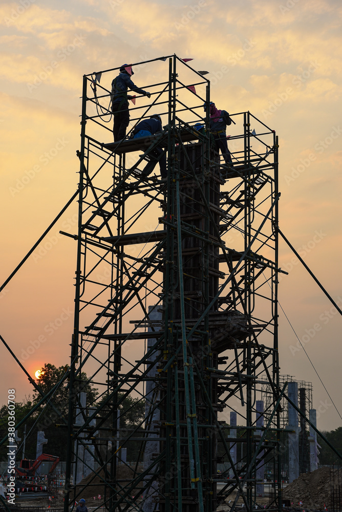 silhouette construction workers are pouring or casting ready mixed concrete column on scaffolding by concrete pocket at construction site